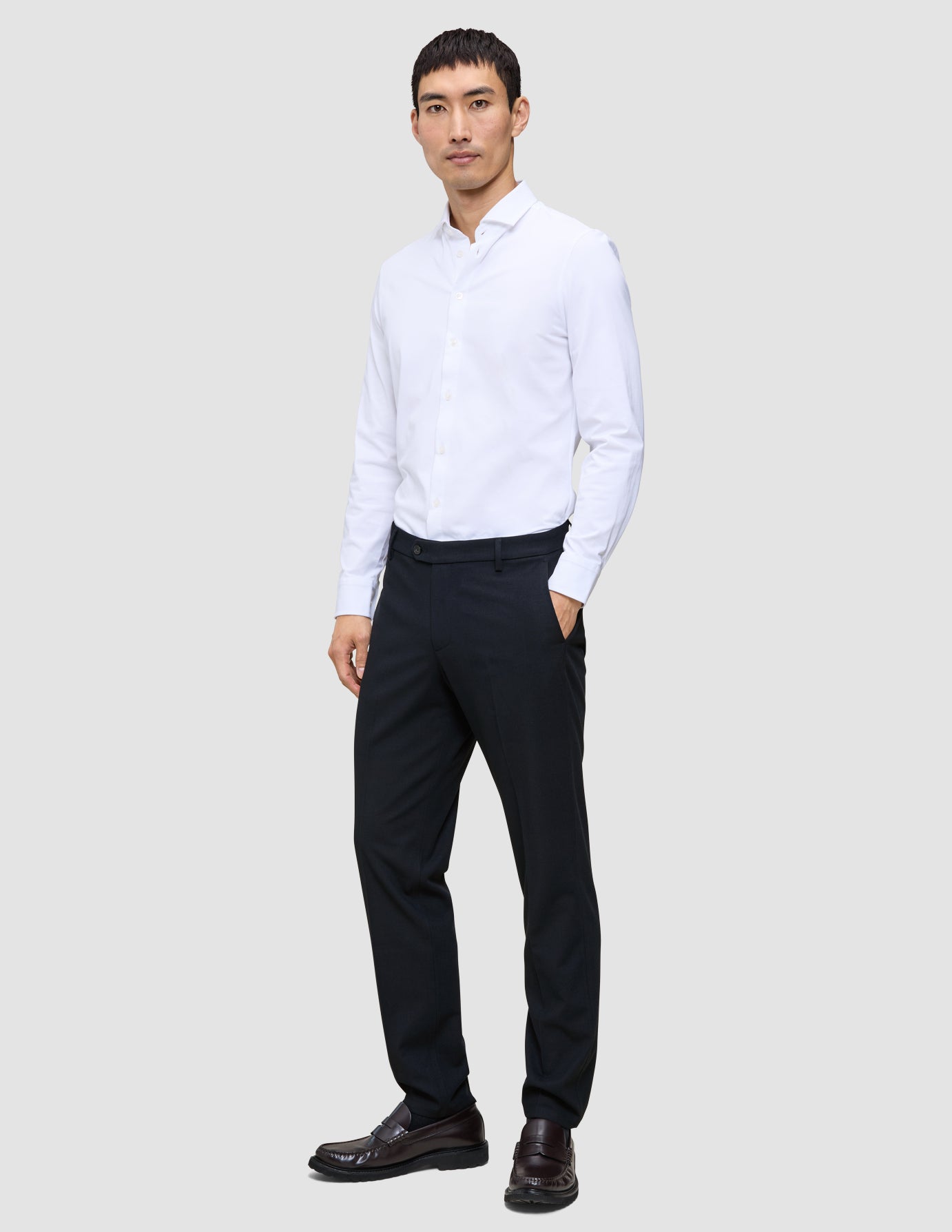 Ein Mann steht mit der Hand in der Tasche da; er trägt ein weißes Hemd und eine Motion Suit-Hose in der Passform Regular in Mitternachtsblau.